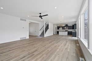 Unfurnished living room featuring sink, ceiling fan with notable chandelier, and light hardwood / wood-style flooring