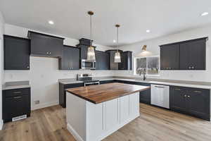 Kitchen with butcher block counters, sink, a center island, appliances with stainless steel finishes, and pendant lighting