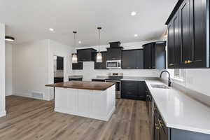 Kitchen featuring sink, appliances with stainless steel finishes, hanging light fixtures, a kitchen island, and light wood-type flooring