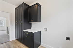 Laundry room with electric dryer hookup, washer hookup, light hardwood / wood-style floors, and cabinets