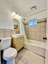 Full bathroom with shower / bath combo, vanity, tile patterned floors, toilet, and tile walls