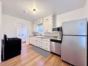 Kitchen featuring appliances with stainless steel finishes, tasteful backsplash, sink, light hardwood / wood-style flooring, and white cabinets