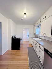 Kitchen with sink, black gas range oven, light hardwood / wood-style flooring, stainless steel dishwasher, and white cabinets