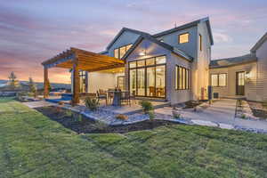 Back house at dusk with a yard, a pergola, and a patio