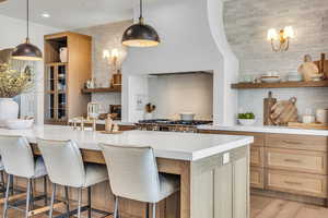 Kitchen with backsplash, an island with sink, a kitchen bar, decorative light fixtures, and white oak flooring