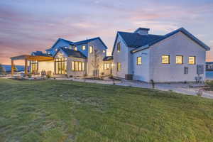 Back house at dusk with a patio, a lawn, central AC unit, and a pergola