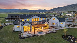 Back house at dusk featuring a mountain view, a yard, an outdoor living space, and a patio