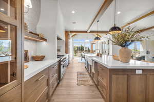 Kitchen featuring hanging light fixtures, beam ceiling, a spacious island, stainless steel range