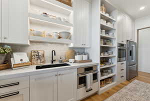 Kitchen with white cabinetry, sink, light stone counters, and stainless steel appliances