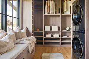 Spacious master closet featuring stacked washing maching and dryer and light hardwood / wood-style floors