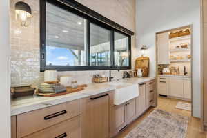 Bar featuring sink, decorative backsplash, light hardwood / wood-style flooring, and light brown cabinets