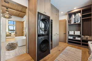 Laundry area featuring wood ceiling, an inviting chandelier, stacked washing maching and dryer, and light hardwood / wood-style floors