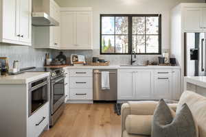 Kitchen in ADU/Mother in law featuring wall chimney exhaust hood, stainless steel appliances, sink, and white cabinets