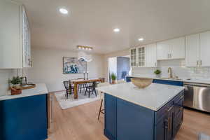 Kitchen with blue cabinetry, a center island, light hardwood / wood-style flooring, stainless steel dishwasher, and white cabinets