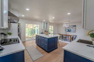 Kitchen featuring white cabinets, blue cabinets, sink, range hood, and light hardwood / wood-style floors