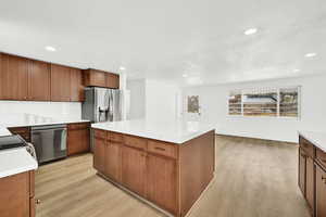 Kitchen with tasteful backsplash, wood-style flooring, a kitchen island, and appliances with stainless steel finishes