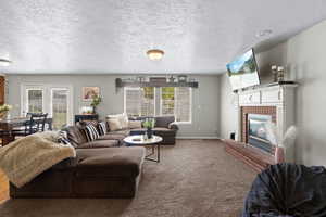 Living room with a textured ceiling, a healthy amount of sunlight, a fireplace, and carpet