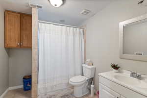 Full bathroom with tile patterned flooring, vanity, toilet, and a textured ceiling