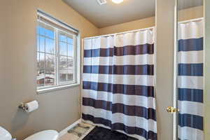 Bathroom with toilet, a shower with shower curtain, and tile patterned floors