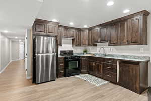 Kitchen with black range with gas stovetop, light hardwood / wood-style flooring, stainless steel refrigerator, and sink