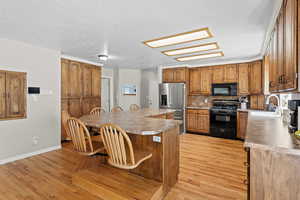 Kitchen featuring black appliances, sink, a skylight, a textured ceiling, and light hardwood / wood-style floors