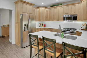 Kitchen with a breakfast bar, light wood-type flooring, stainless steel appliances, and light brown cabinetry