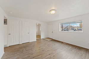 Unfurnished bedroom with a textured ceiling, light hardwood / wood-style floors, and multiple closets