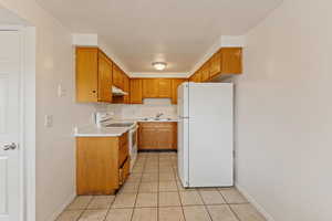 Kitchen with light tile patterned flooring, sink, white appliances, and a textured ceiling