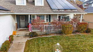 View of exterior entry featuring solar panels, a porch, and a lawn