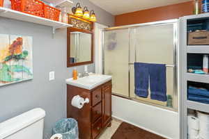 Full bathroom with shower / bath combination with glass door, vanity, and toilet