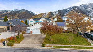 View of property featuring a mountain view, a front lawn, a garage, and solar panels