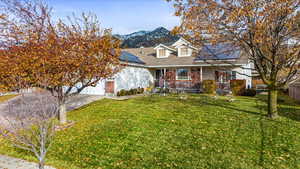 View of front of property featuring covered porch, solar panels, a front lawn, and a mountain view