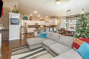 Living room with ceiling fan, dark hardwood / wood-style flooring, and vaulted ceiling