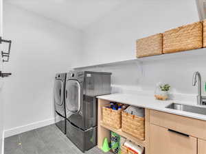 Laundry area with washer and clothes dryer, sink, dark tile patterned floors, and cabinets