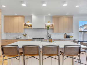 Kitchen featuring light brown cabinetry, stainless steel range oven, light hardwood / wood-style flooring, and an island with sink