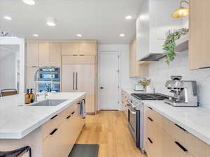 Kitchen with light brown cabinetry, sink, decorative light fixtures, high quality appliances, and light hardwood / wood-style floors