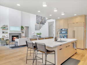 Kitchen with a tile fireplace, sink, paneled built in fridge, light hardwood / wood-style floors, and a kitchen island with sink