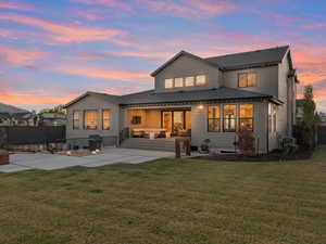 Back house at dusk with outdoor lounge area, cooling unit, a patio, and a lawn