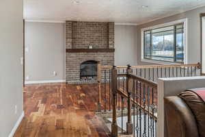 Living room with crown molding, wood-type flooring, a textured ceiling, and a brick fireplace