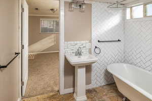 Bathroom featuring a textured ceiling, a tub, tile walls, and a healthy amount of sunlight