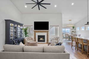 Living room with light wood finished floors, recessed lighting, a high ceiling, a glass covered fireplace, and ceiling fan