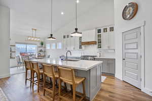 Kitchen featuring an island with sink, glass insert cabinets, hanging light fixtures, light countertops, and a sink