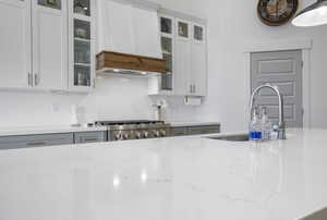 Kitchen with tasteful backsplash, glass insert cabinets, a sink, light stone countertops, and range