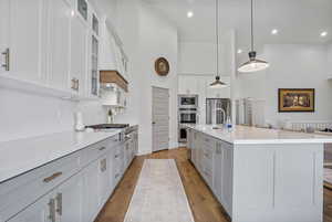 Kitchen with a kitchen island with sink, a towering ceiling, white cabinetry, appliances with stainless steel finishes, and pendant lighting