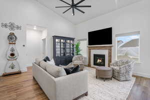 Living area with baseboards, a glass covered fireplace, ceiling fan, wood finished floors, and high vaulted ceiling