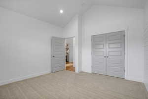 Unfurnished bedroom featuring baseboards, high vaulted ceiling, a closet, and light colored carpet