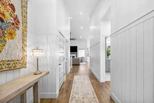 Hall featuring light wood-type flooring, a decorative wall, a towering ceiling, and recessed lighting