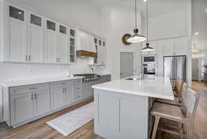 Kitchen featuring stainless steel appliances, hanging light fixtures, glass insert cabinets, a sink, and an island with sink