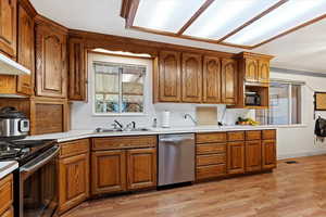 Kitchen with light wood-type flooring, sink, appliances with stainless steel finishes, and ornamental molding