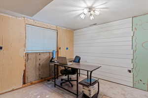 Office area featuring a textured ceiling, concrete floors, and wood walls